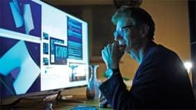 Man with glasses looks at a computer screen, likely at the Financial Ratios and Operational Benchmarking Survey report from FMA.